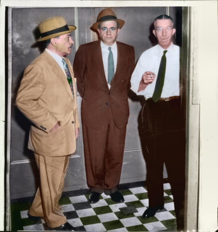 three men standing next to each other in front of a door wearing suits and ties