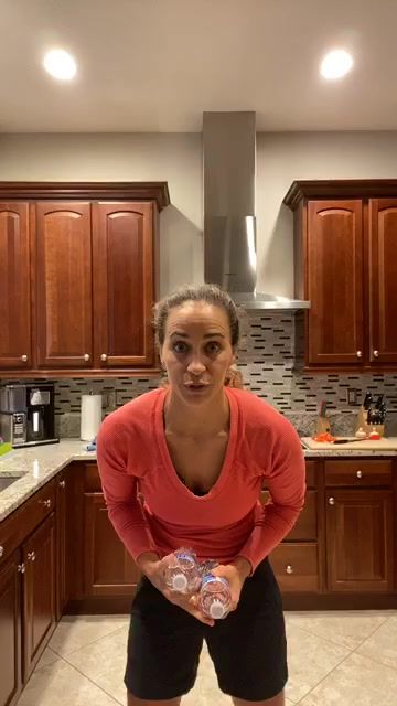 a woman standing in a kitchen holding two water bottles