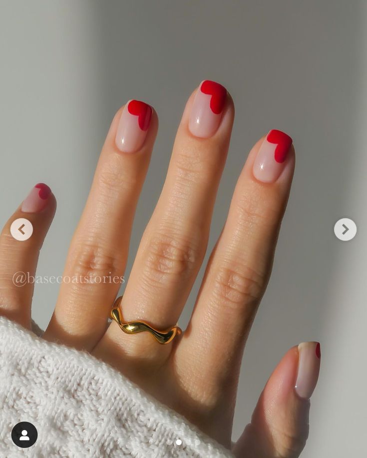 a woman's hand with red and white nail polish on it, holding a gold ring