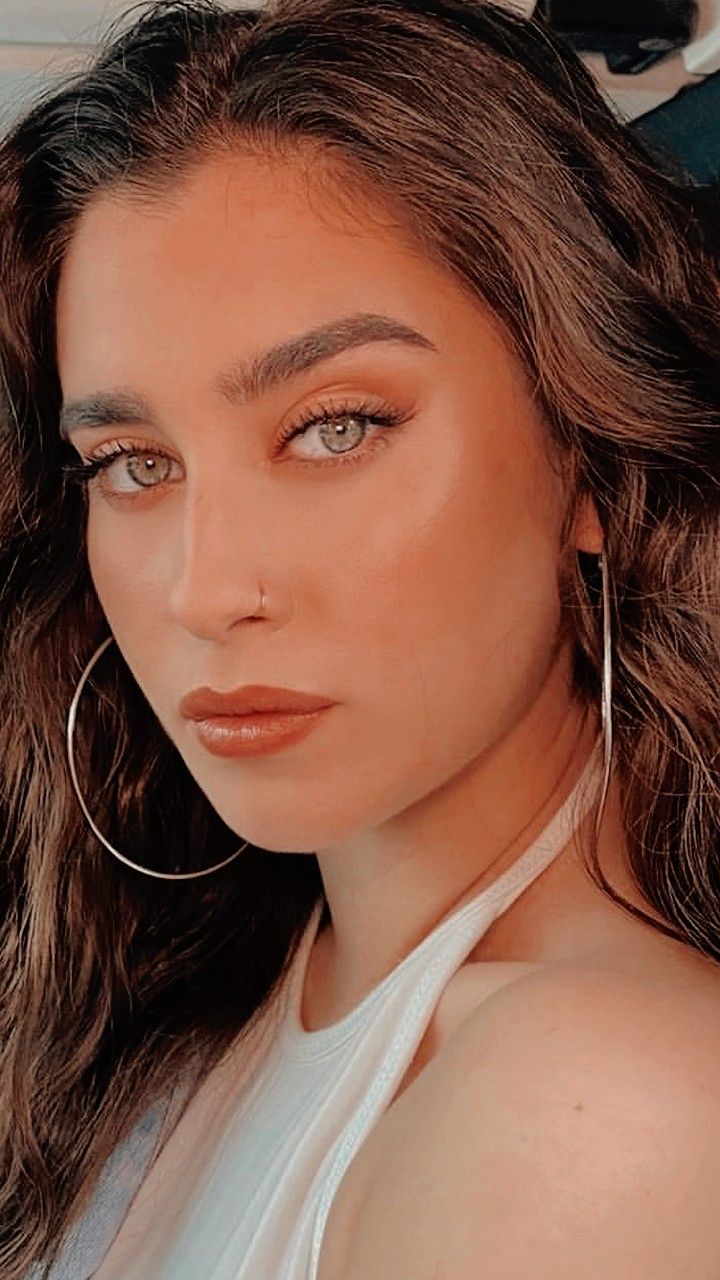 a woman wearing large hoop earrings and a white tank top is looking at the camera