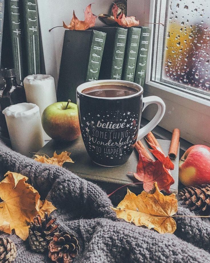 a cup of coffee sitting on top of a table next to books and autumn leaves