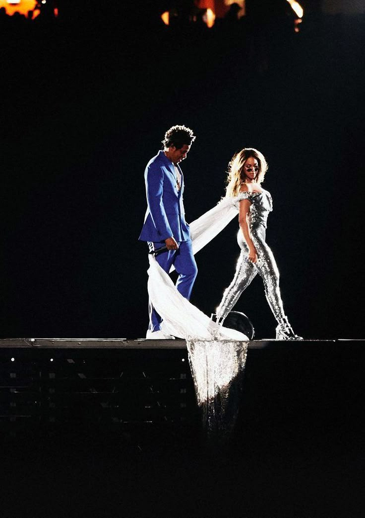 two people dressed in white and blue on stage with one holding the other's hand