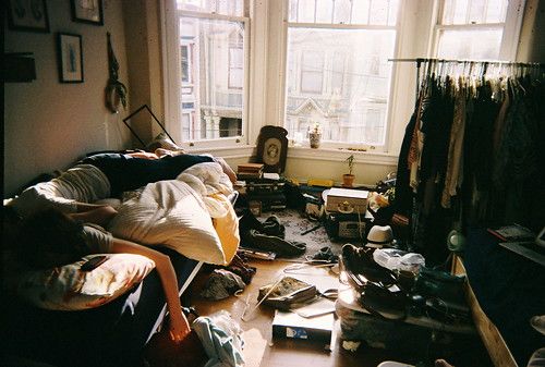 an unmade bed in a messy room with lots of clutter on the floor