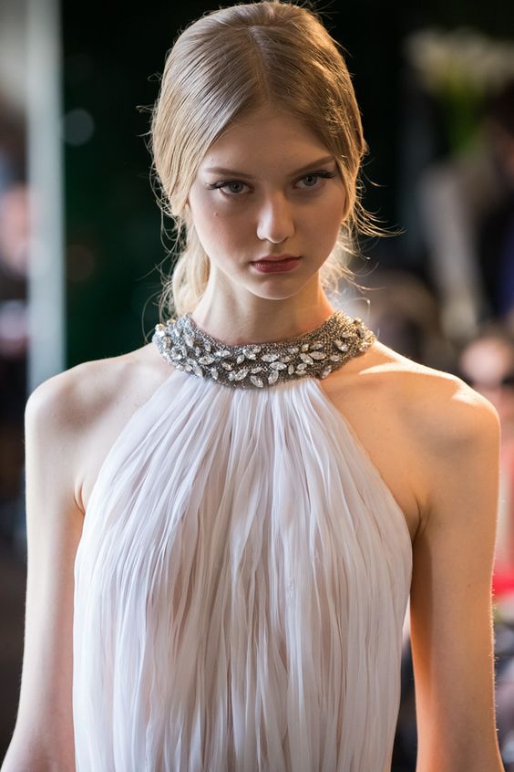 a woman in a white dress with a necklace on her neck and hair pulled back