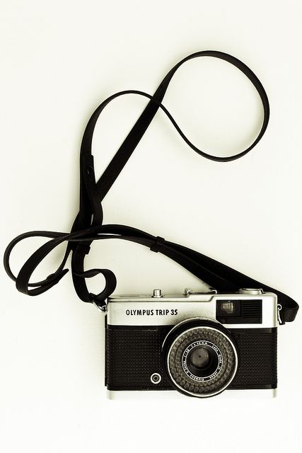 an old fashioned camera sitting on top of a white table next to a black strap