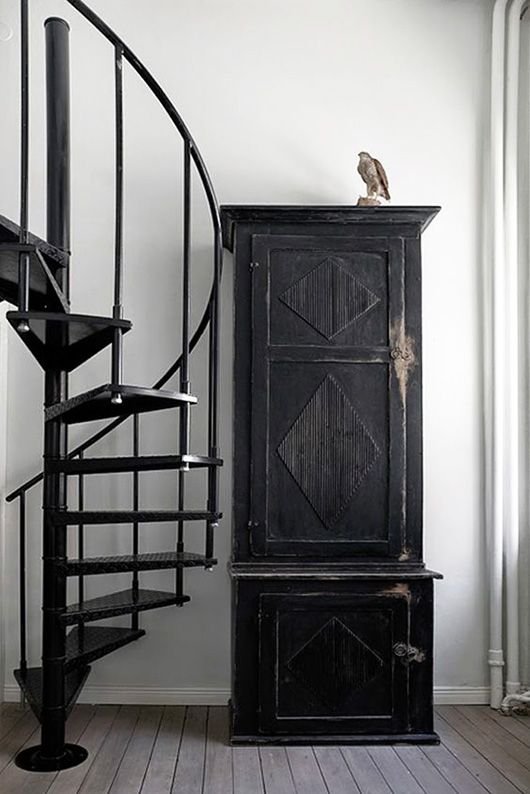 a bird sitting on top of a black cabinet next to a spiral stair case in a white room