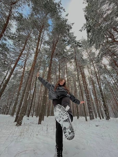 a woman is doing a trick on her snowboard in the middle of a snowy forest