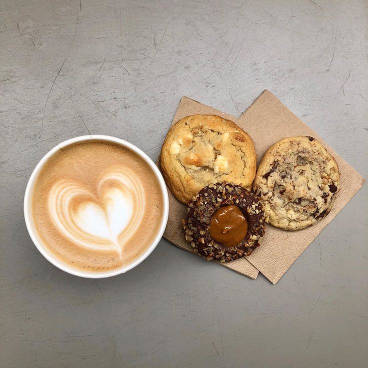 a cup of coffee and some cookies on a napkin with a heart drawn in the foam