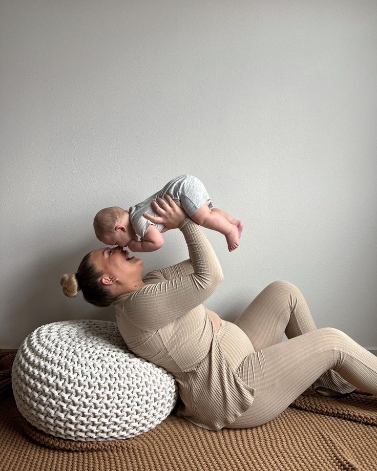 a woman holding a baby while laying on top of a bean bag chair next to a wall