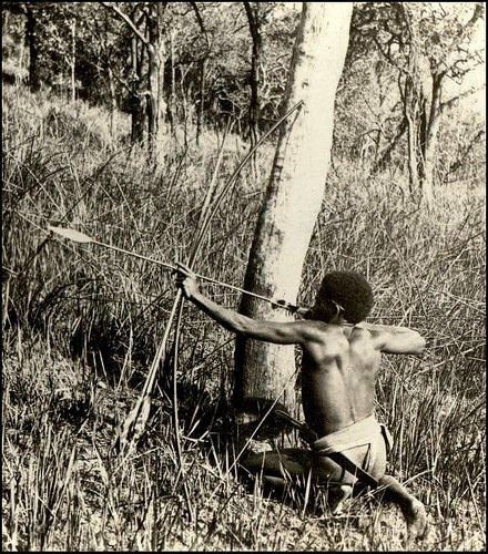 an old photo of a shirtless man holding a bow and arrow in the woods