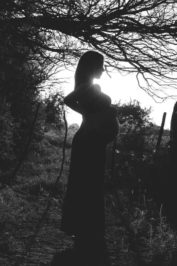 a pregnant woman standing under a tree in the sun with her hands on her hips