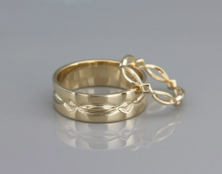 two gold wedding bands with intertwined design on them, sitting next to each other