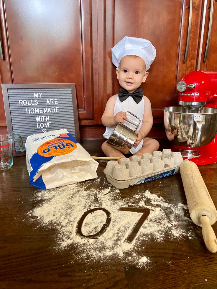 a baby is sitting on the kitchen counter with flour and an egg carton in front of him