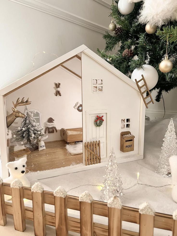 a doll house is set up in front of a christmas tree with snow on the ground