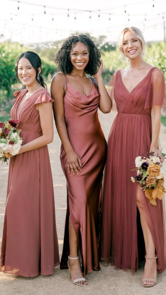 three bridesmaids pose for a photo in front of an outdoor string - light