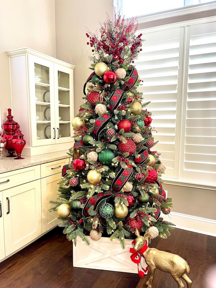 a decorated christmas tree in a kitchen with red and green ornaments on the top, next to a gold deer figurine