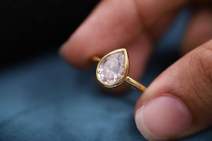 a close up of a person's hand holding a ring with a diamond on it