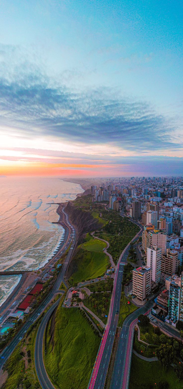 an aerial view of a city and the ocean at sunset, with cars driving on the road