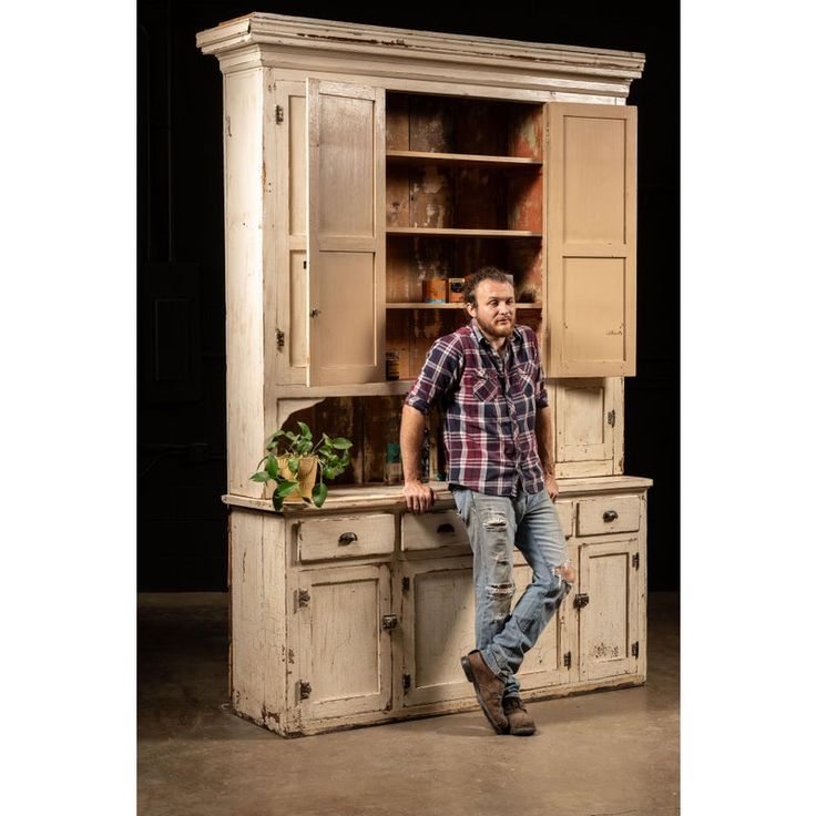 a man standing next to an old white cabinet with glass doors and drawers on it