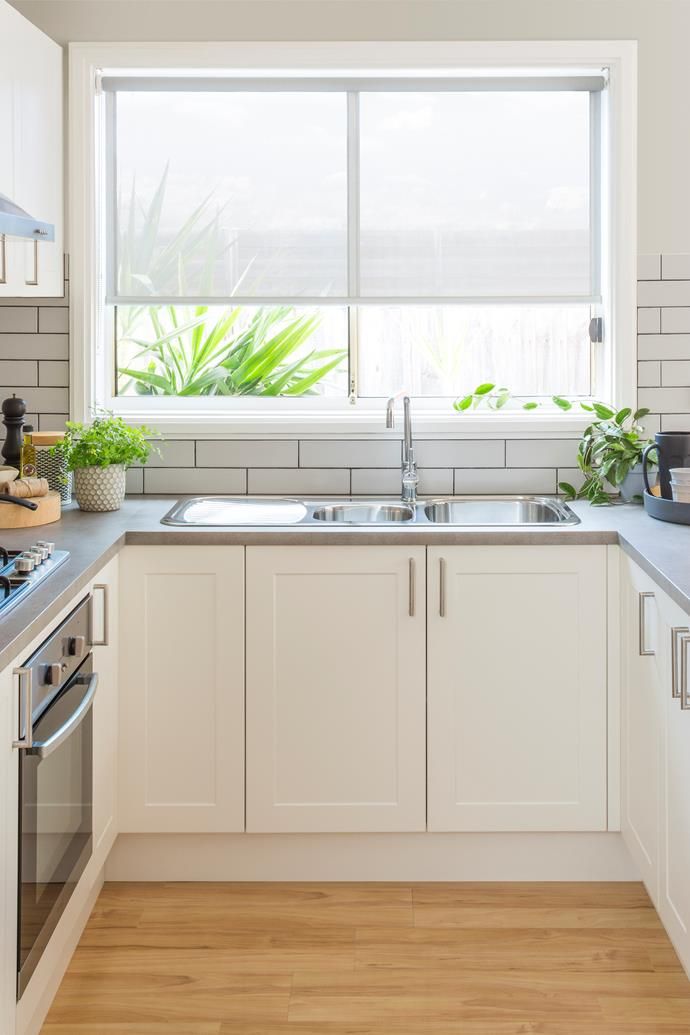 a kitchen with white cabinets and wood flooring next to a window that has plants on it