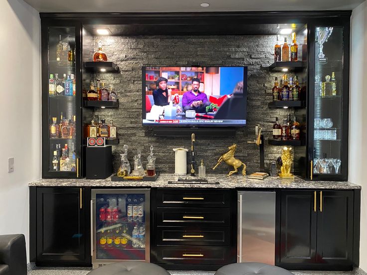 an entertainment center with black cabinets and shelves filled with bottles, liquors and other items