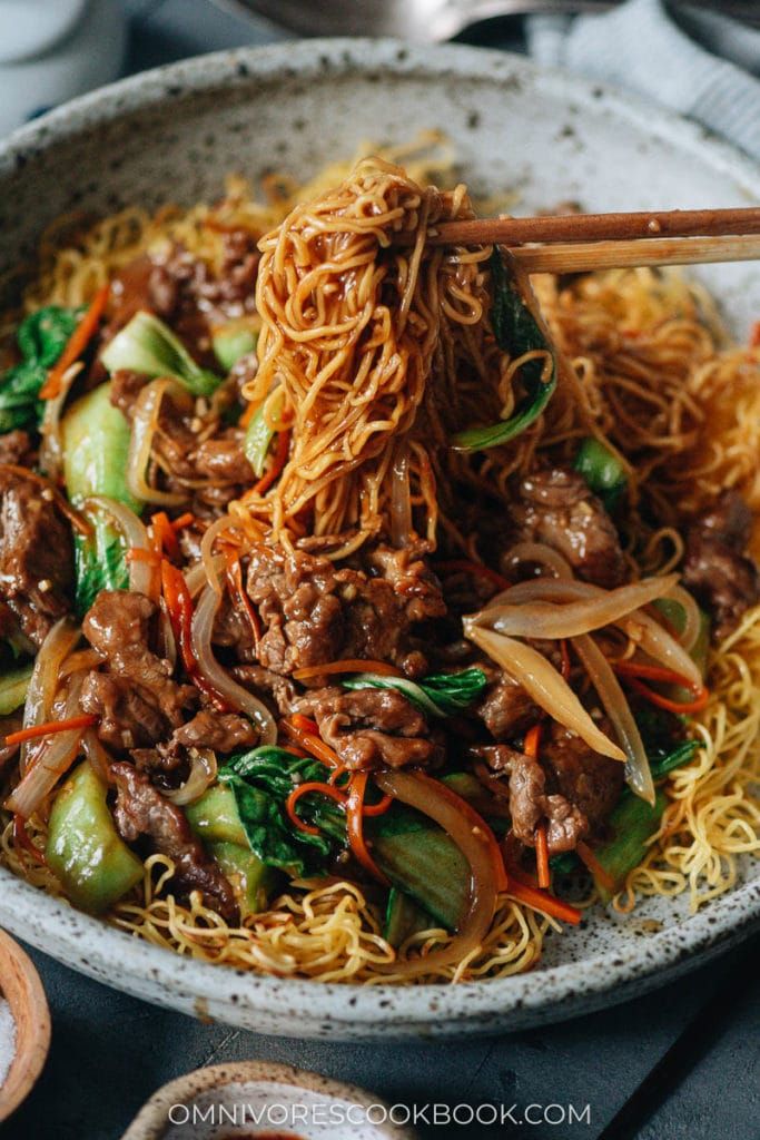 a white bowl filled with noodles and meat on top of a table next to chopsticks