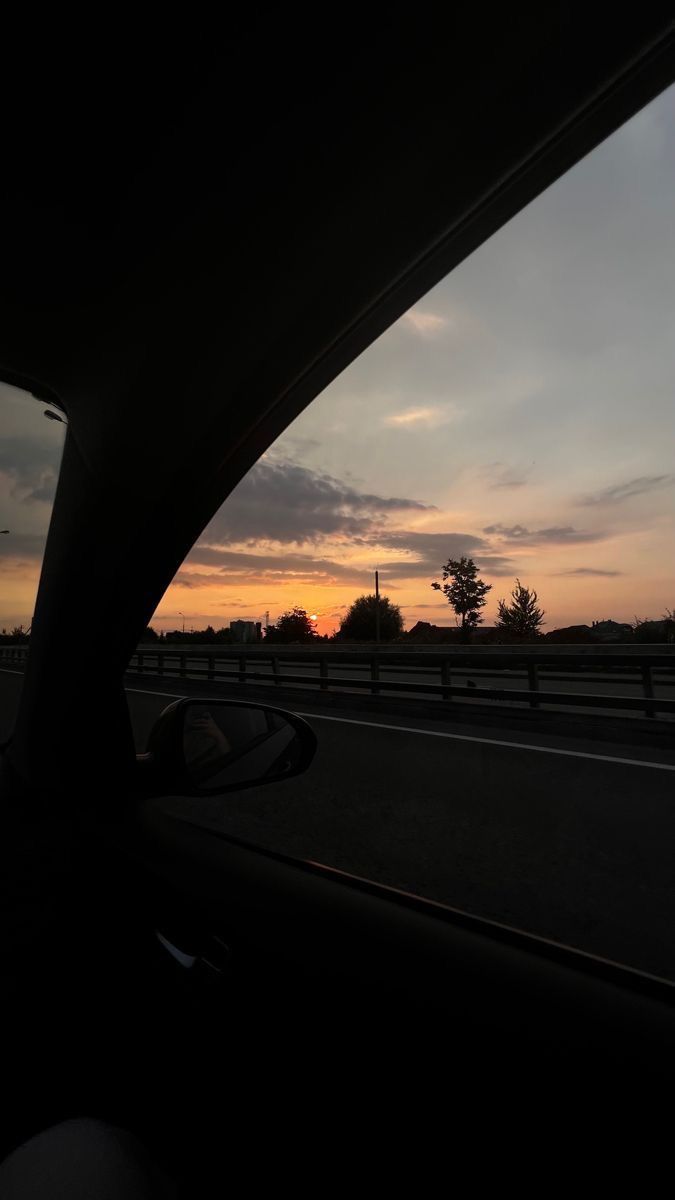 the sun is setting over an empty highway with cars driving on one side and trees in the other