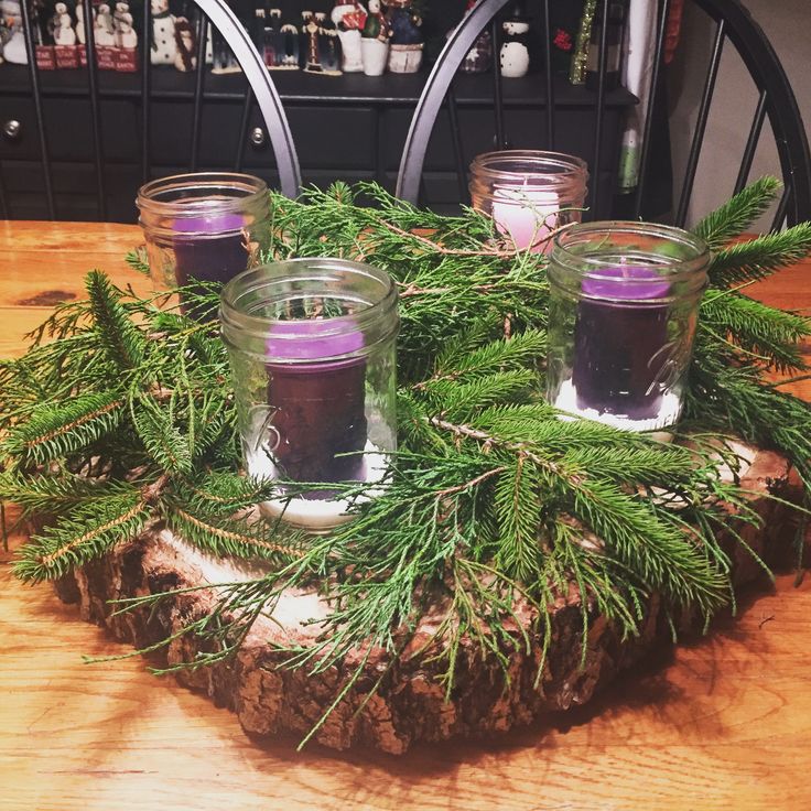 some candles are sitting on top of a piece of wood with greenery around it