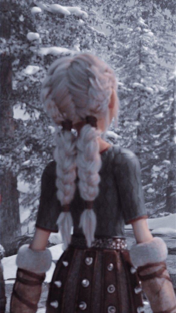 a girl with long hair and gloves standing in front of snow covered trees looking at the ground