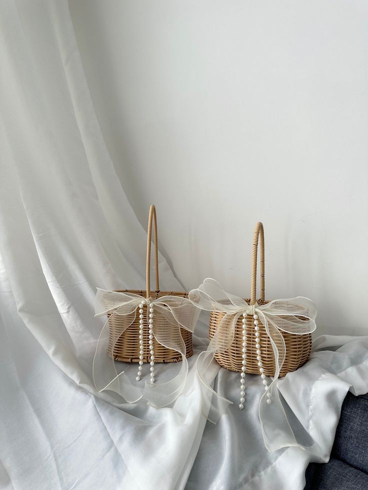 two wicker baskets sitting on top of a white cloth covered bed next to each other