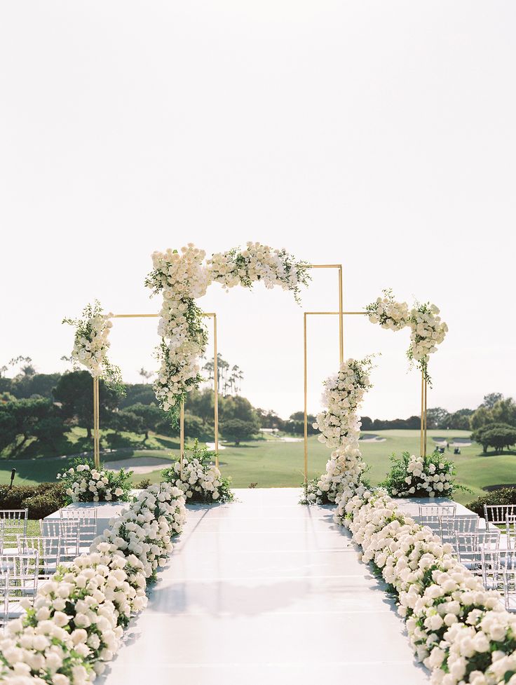 an outdoor ceremony setup with white flowers and greenery on either side of the aisle