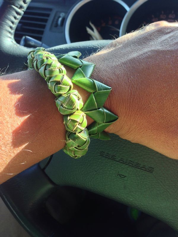 a person wearing a bracelet made out of green leaves on their arm in a car