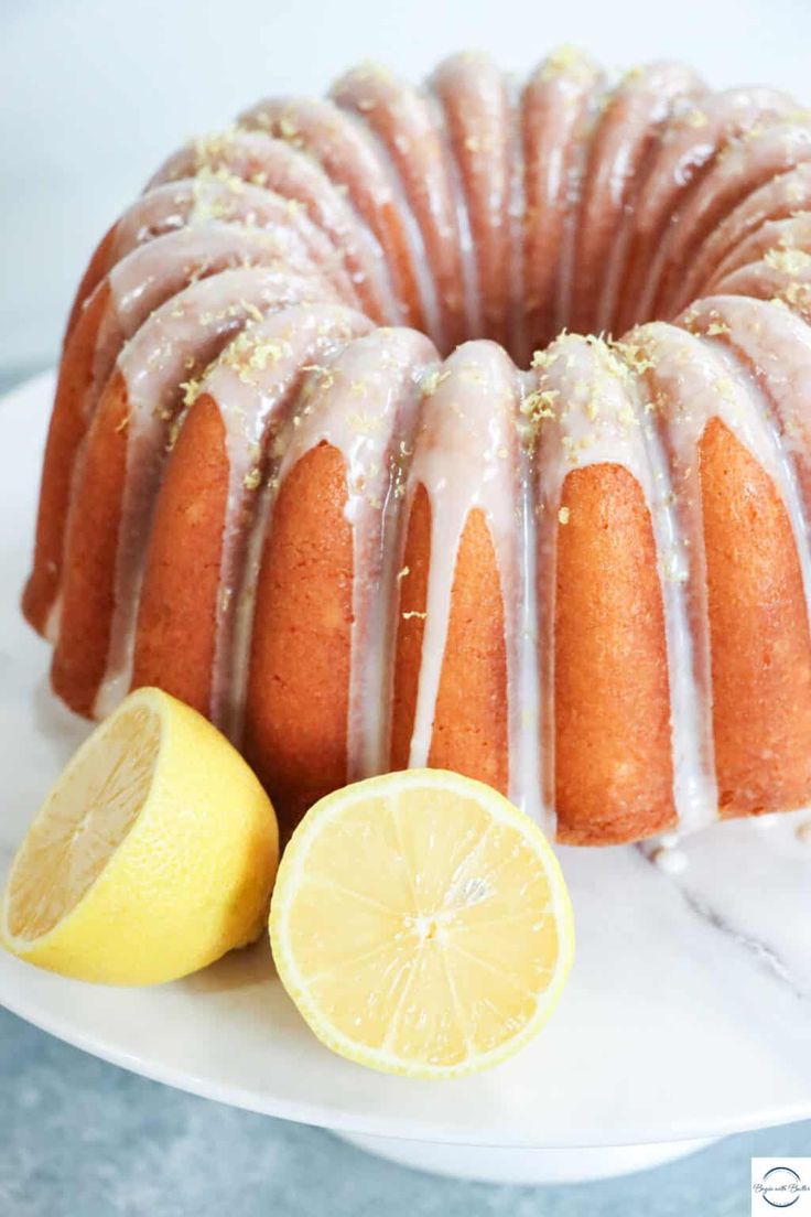 a lemon bunt cake on a white plate next to sliced lemons and a slice of lemon