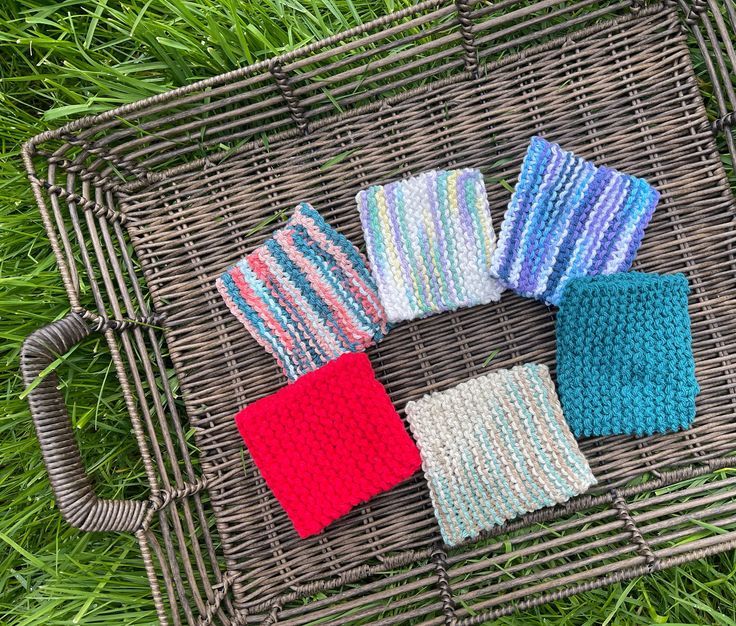 four knitted napkins sitting on top of a wicker basket in the grass