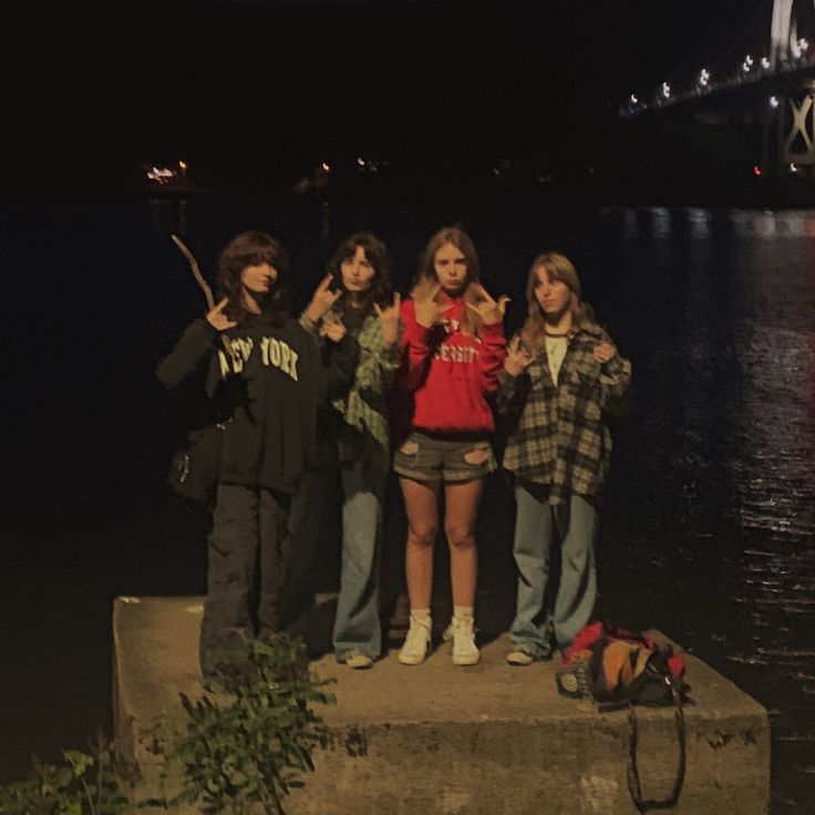 four young people standing on the edge of a concrete block in front of a body of water