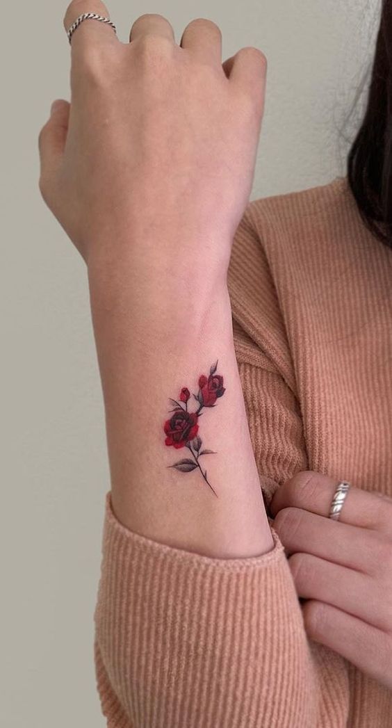 a woman's arm with a small red rose tattoo on the left side of her wrist