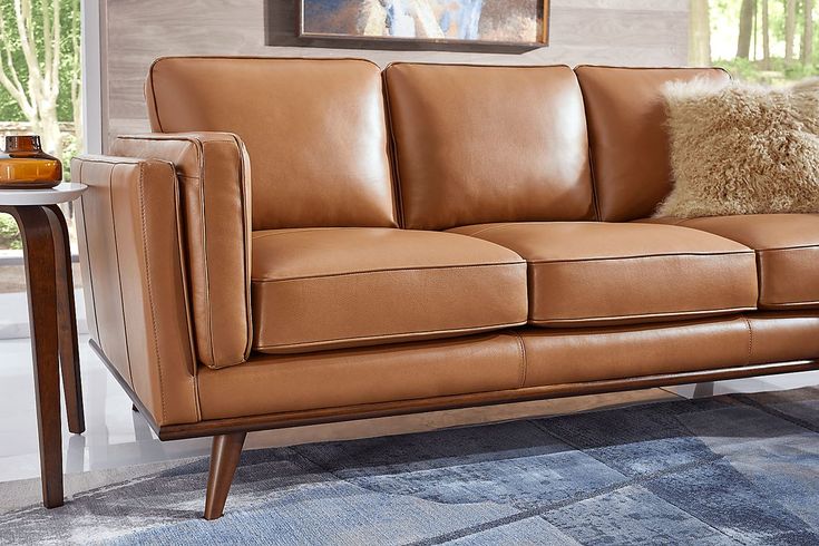 a tan leather couch with pillows on it in a living room area next to a table