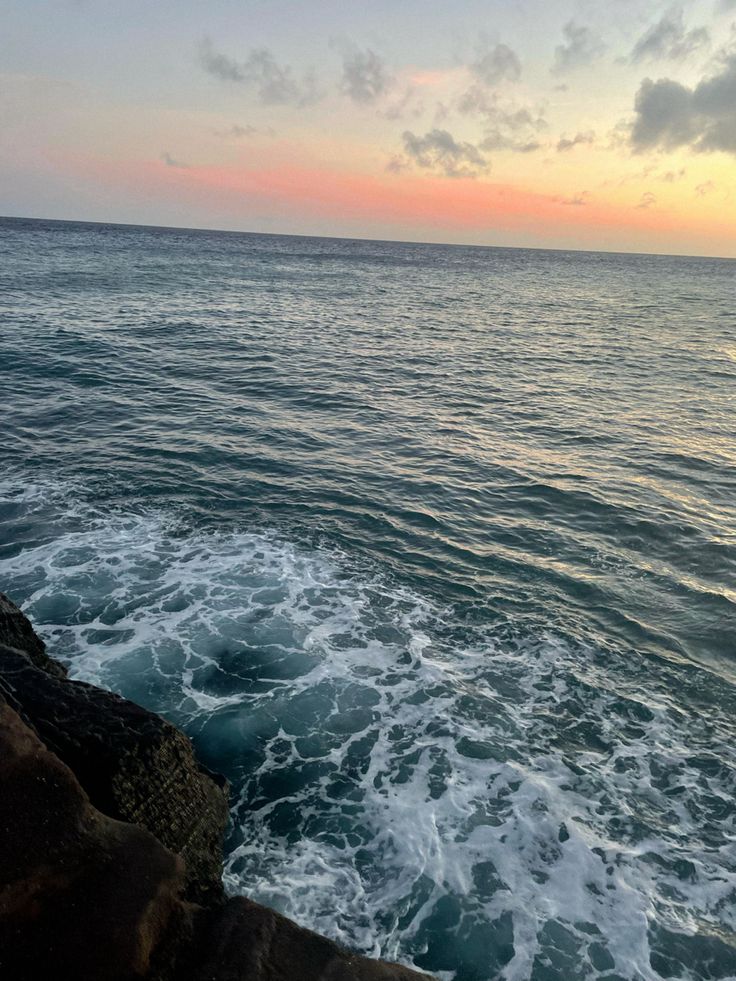 the ocean with waves coming in to shore at sunset or sunrise, as seen from rocky shoreline