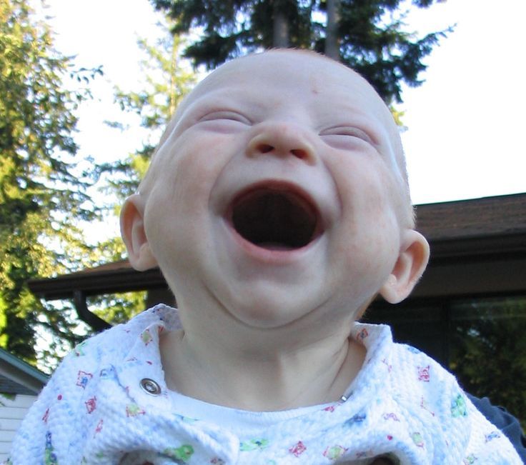 a baby laughing with its mouth open in front of a tree and house behind it