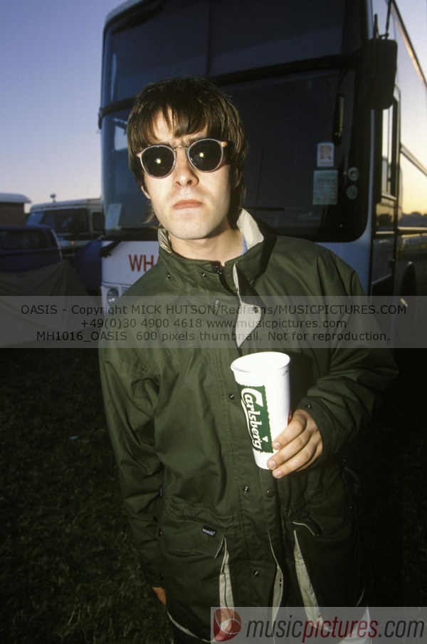 a man wearing sunglasses and holding a coffee cup in front of a large bus at sunset