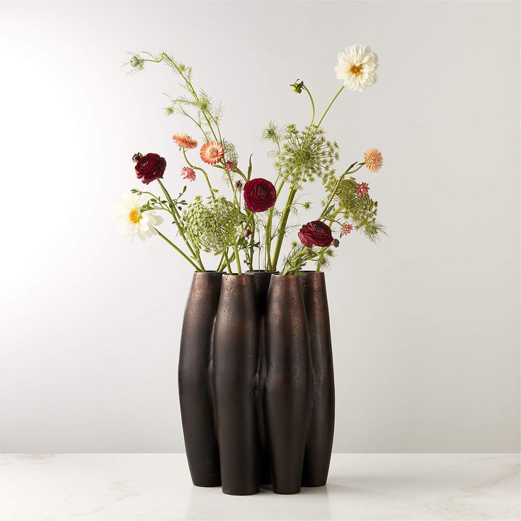 three black vases with flowers in them on a white countertop against a wall