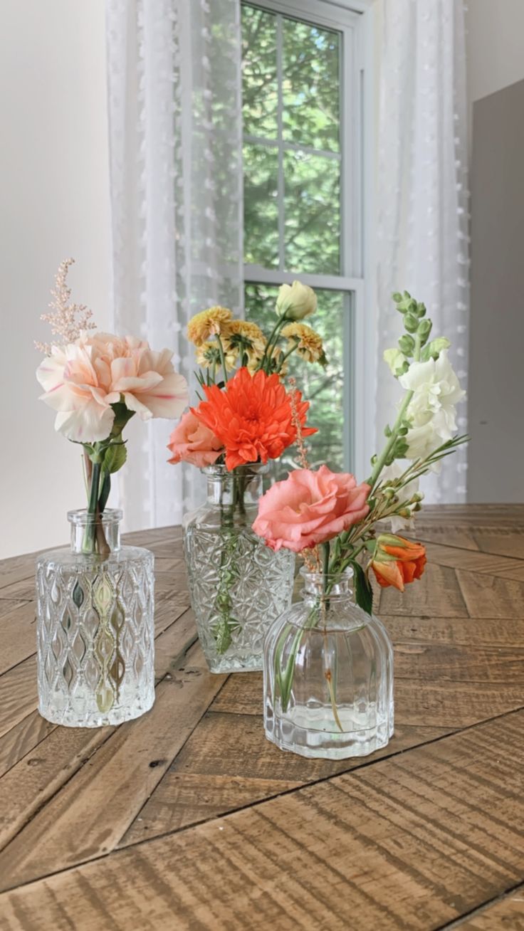 three glass vases with flowers in them sitting on a table next to a window