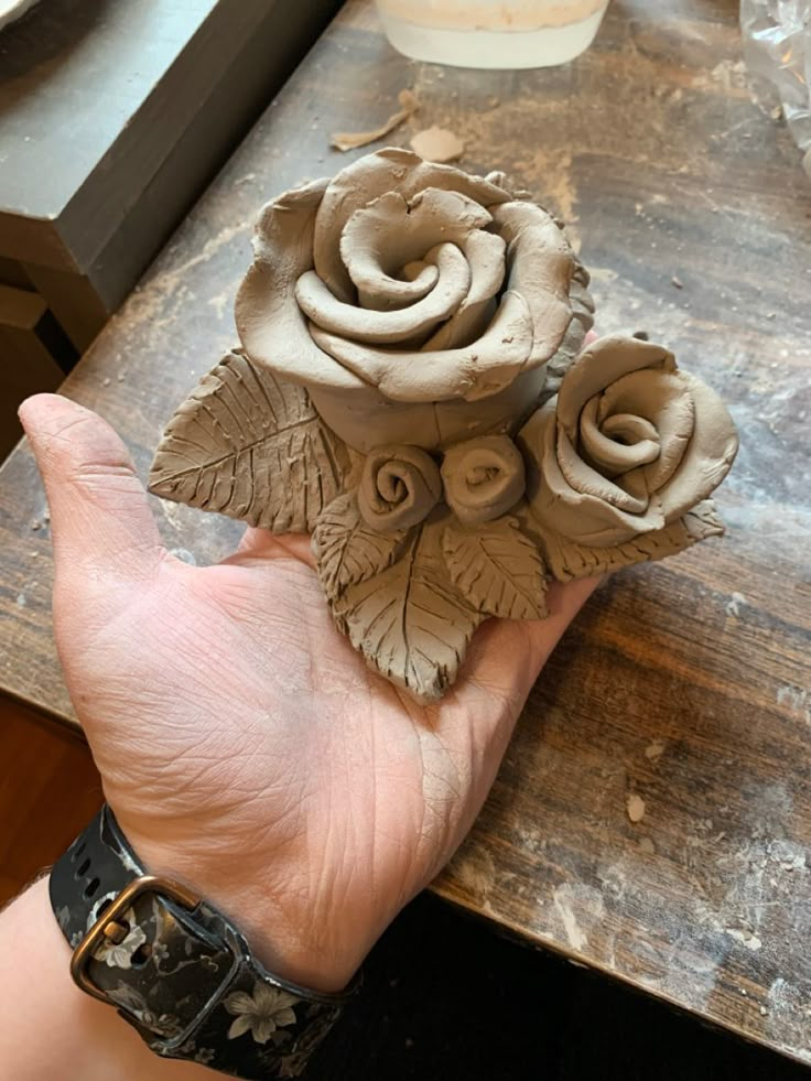 a hand holding a clay rose on top of a wooden table