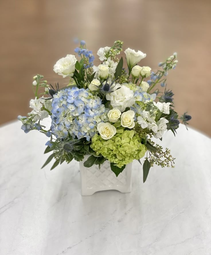 a vase filled with white and blue flowers on top of a marble tablecloth covered table