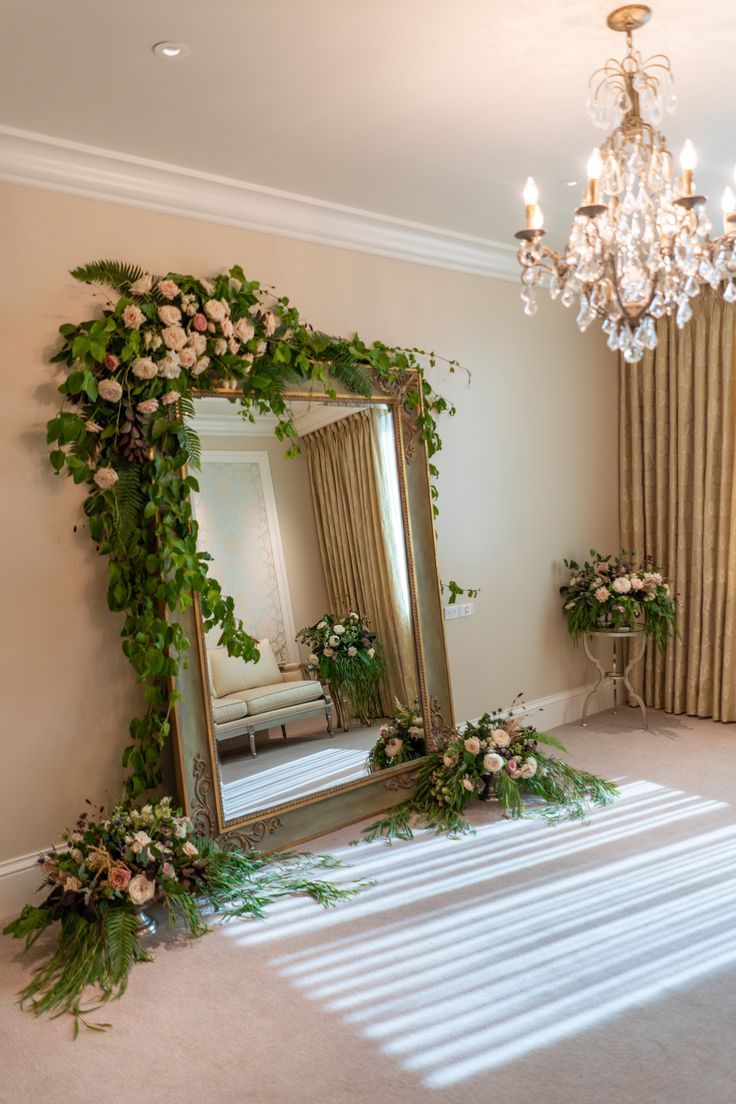 a mirror sitting on top of a floor next to a table with flowers and greenery