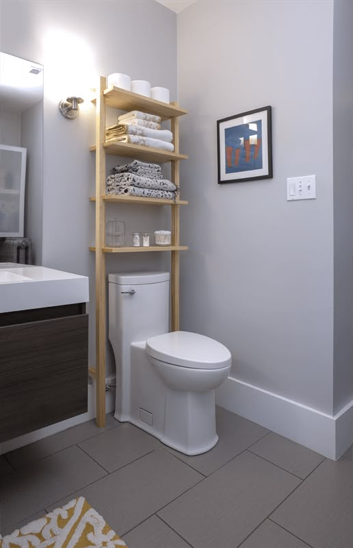 a white toilet sitting in a bathroom next to a wooden shelf filled with folded towels