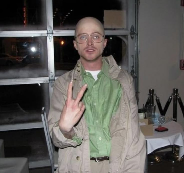 a man with glasses making the peace sign in front of a table and window at night