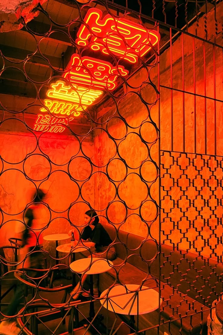 a man sitting at a table in front of a neon sign behind a wire fence