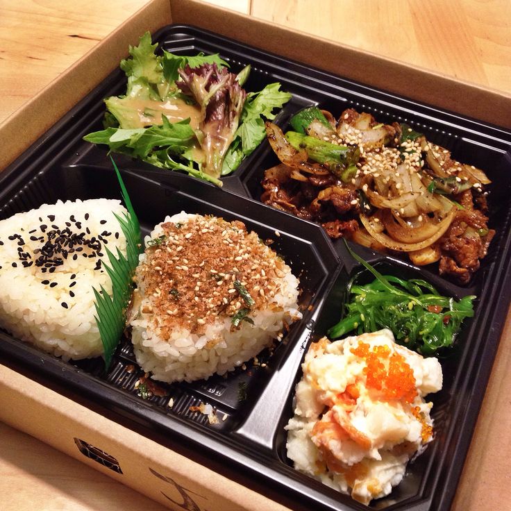 a bento box filled with rice, meat and veggies on top of a wooden table