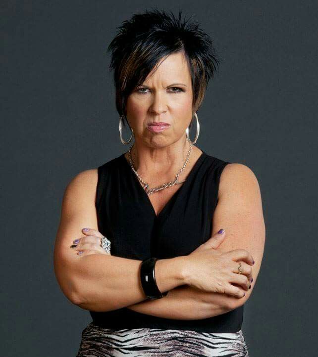 a woman with her arms crossed wearing a black top and zebra print skirt is looking at the camera